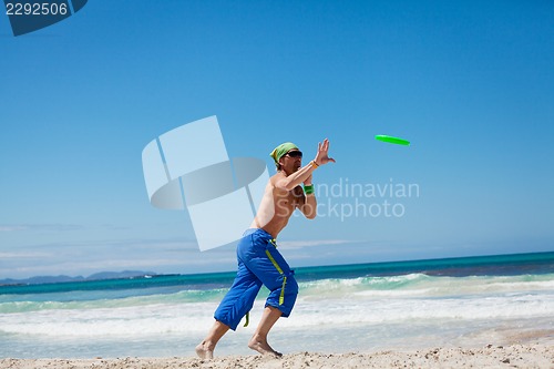 Image of attractive man playing frisby on beach in summer