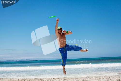 Image of attractive man playing frisby on beach in summer