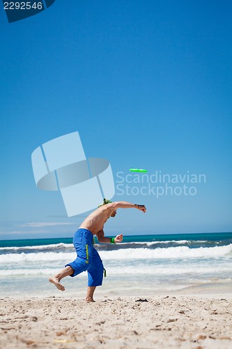 Image of attractive man playing frisby on beach in summer