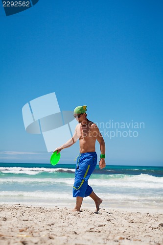 Image of attractive man playing frisby on beach in summer