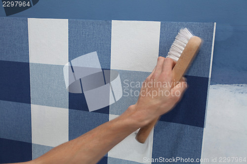 Image of decorator hanging wallpaper with work tool in motion