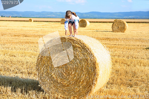 Image of small rural girl on the straw after harvest field with straw bal