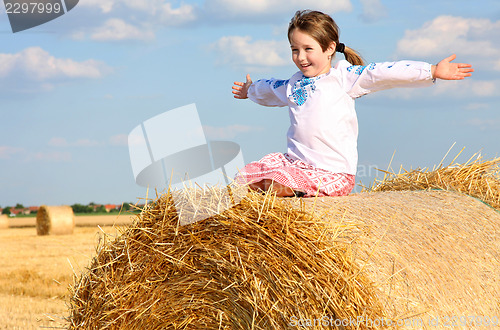 Image of small rural girl on the straw after harvest field with straw bal