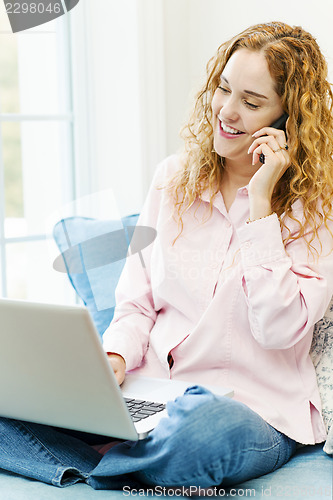 Image of Woman talking on phone and using computer