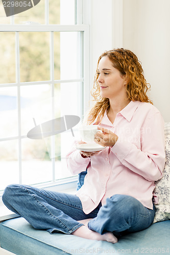 Image of Woman relaxing by the window with coffee