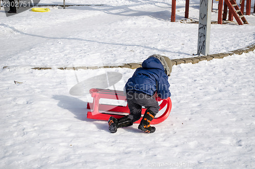 Image of boy with blue jacket knelt down to red sleigh  
