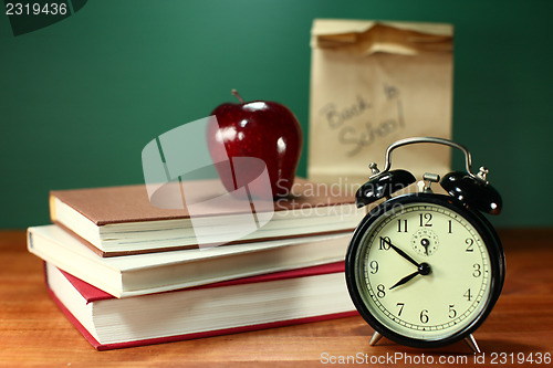 Image of Lunch, Apple, Books and Clock on Desk at School