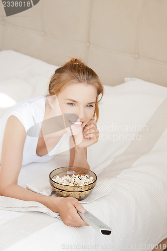 Image of happy teenage girl with TV remote and popcorn