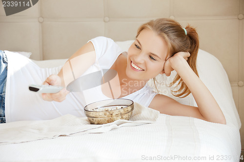 Image of happy teenage girl with TV remote and popcorn