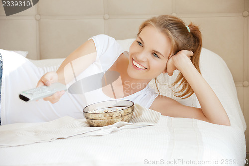 Image of happy teenage girl with TV remote and popcorn