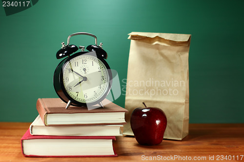 Image of Lunch, Apple, Books and Clock on Desk at School