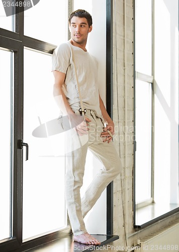 Image of handsome man standing on the windowsill