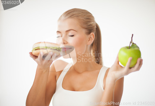 Image of woman smelling hamburger and holding apple