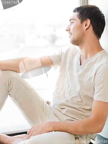 Image of man in casual clothes sitting on the windowsill