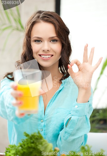 Image of woman holding glass of juice and showing ok sign