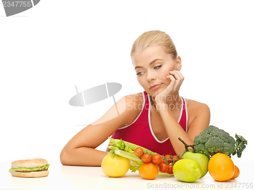 Image of doubting woman with fruits and hamburger