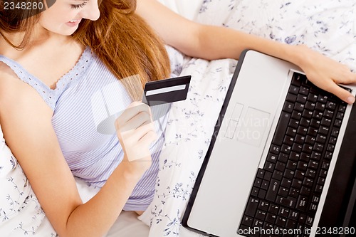 Image of girl sitting in bed and shopping online with credit card