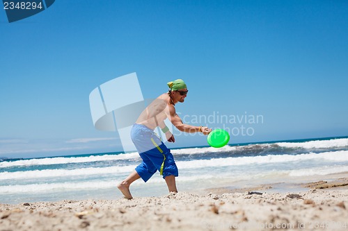 Image of attractive man playing frisby on beach in summer