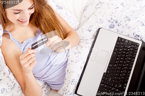 Image of girl sitting in bed and shopping online with credit card