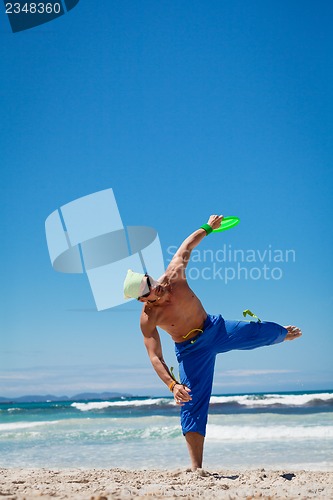 Image of attractive man playing frisby on beach in summer