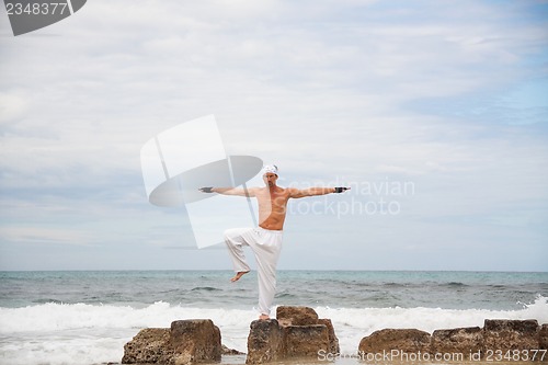 Image of healthy man doing pilates yoga meditation on beach summer