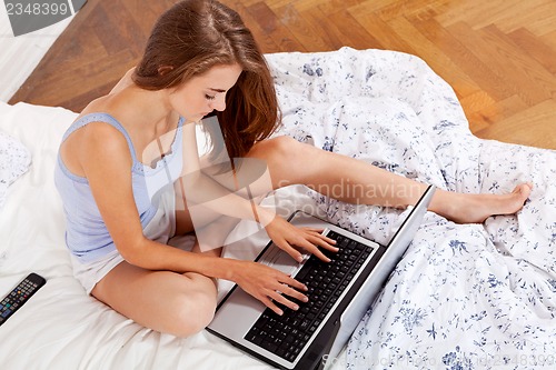 Image of smiling woman sitting on bed with notebook