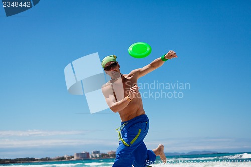 Image of attractive man playing frisby on beach in summer