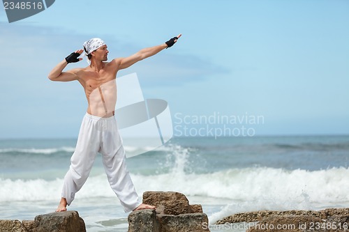 Image of healthy man doing pilates yoga meditation on beach summer