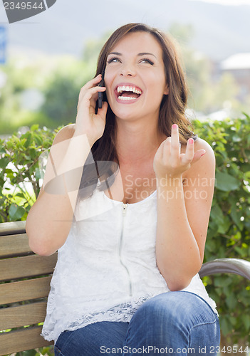 Image of Young Adult Female Talking on Cell Phone Outdoors on Bench