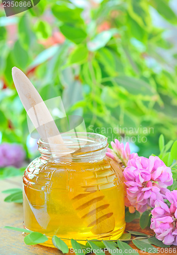 Image of glass jar full of honey and stick with acacia pink and white flo