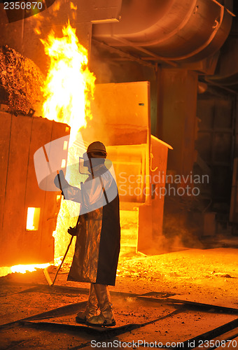 Image of A steel worker takes a sample from oven