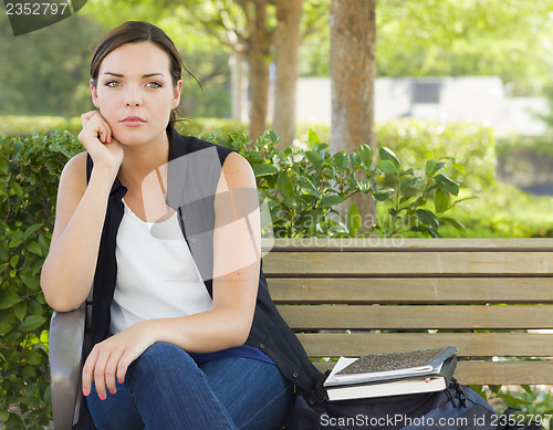 Image of Melancholy Young Adult Woman Sitting on Bench Next to Books
