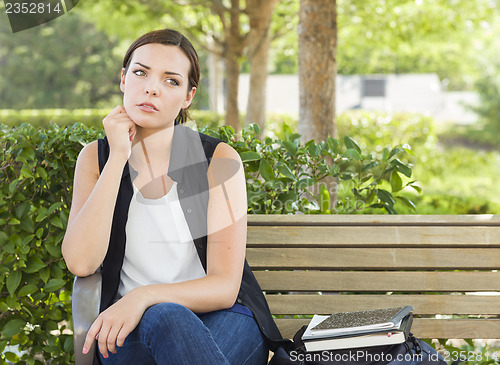 Image of Melancholy Young Adult Woman Sitting on Bench Next to Books
