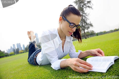 Image of Young woman reading a book in the park