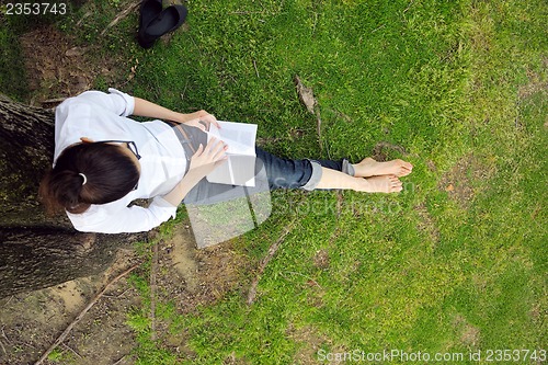 Image of Young woman reading a book in the park