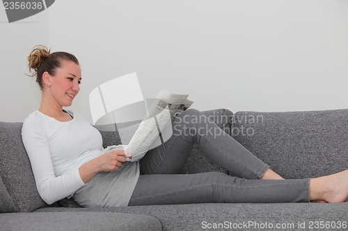 Image of Woman relaxing on a sofa with a newspaper