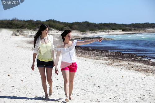 Image of Two attractive woman walking on a beach