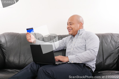 Image of Handsome man holding credit card and using laptop 