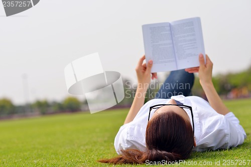 Image of Young woman reading a book in the park