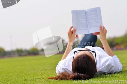 Image of Young woman reading a book in the park