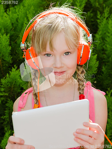 Image of Cute girl with tablet pc listening music in headphones