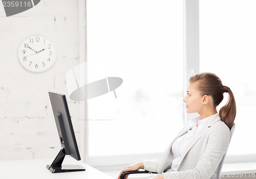 Image of businesswoman looking at wall clock in office