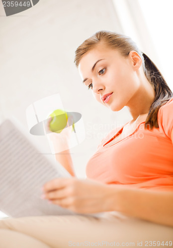 Image of woman with green apple reading newspaper at home