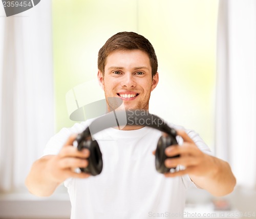 Image of young smiling man offering headphones at home