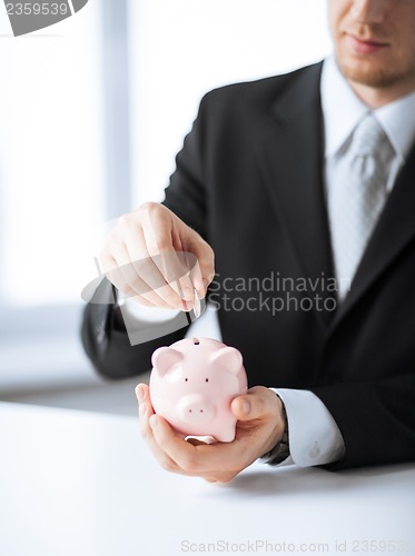 Image of man putting coin into small piggy bank