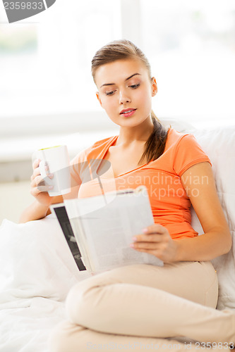 Image of woman with cup of coffee reading magazine at home