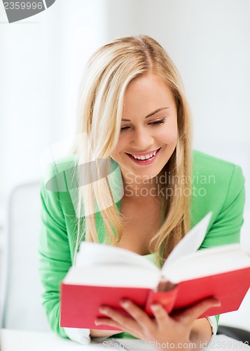 Image of smiling young woman reading book at school