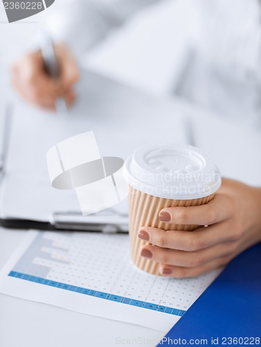 Image of woman filling in form and drinking coffee