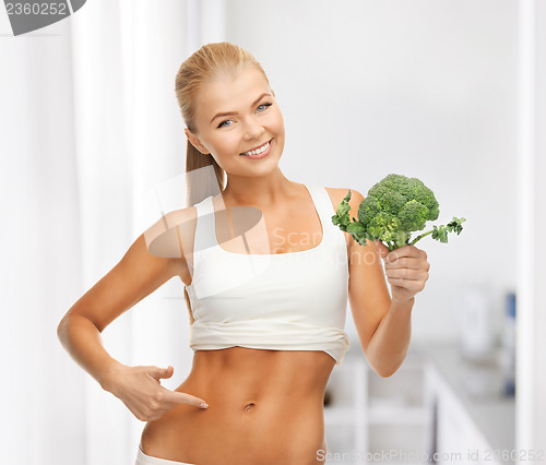 Image of woman pointing at her abs and holding broccoli