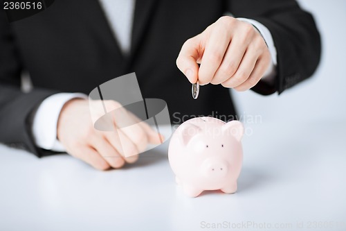 Image of man putting coin into small piggy bank